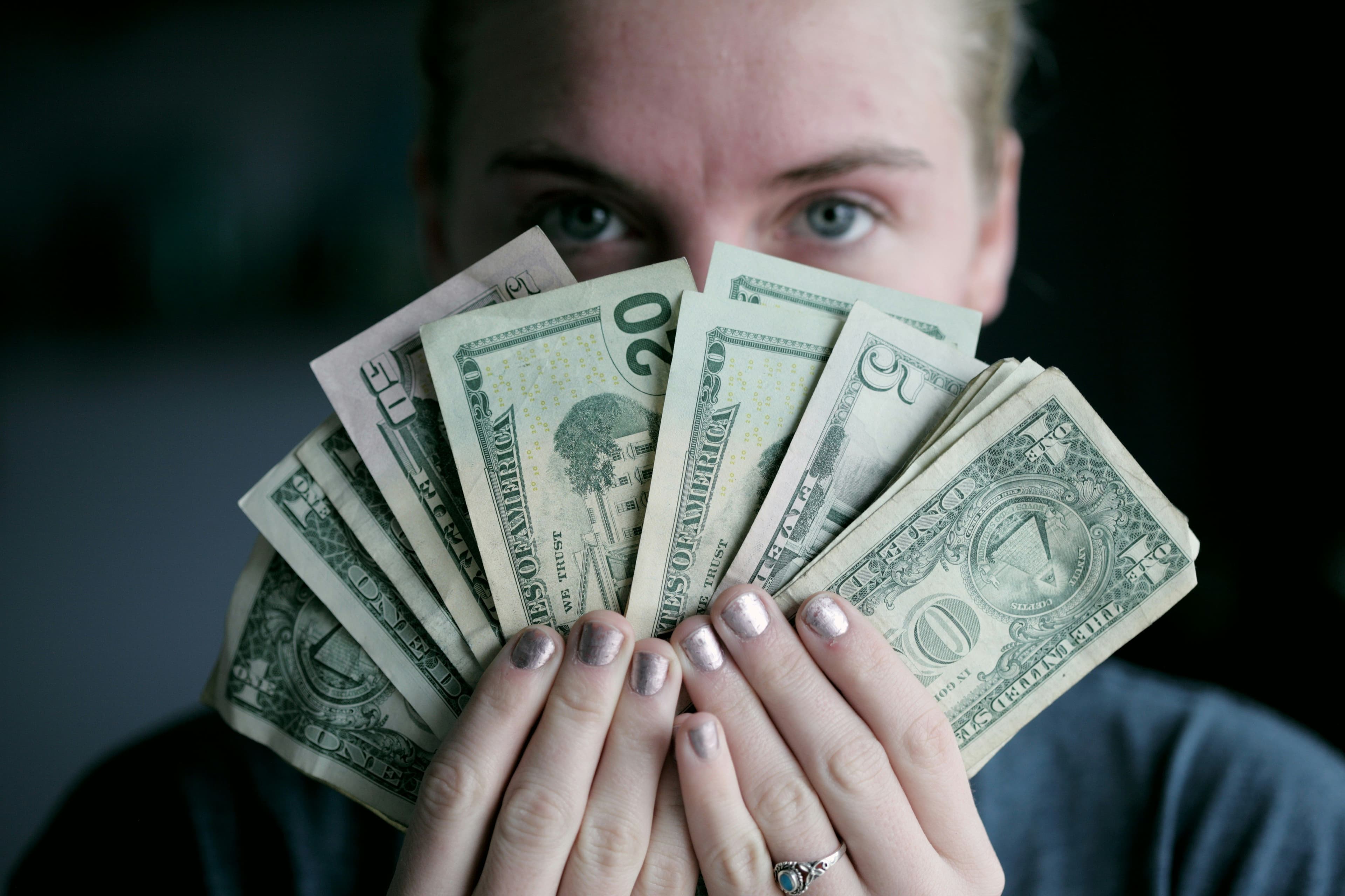 A person holding burning U.S. dollar bills with a plain background.