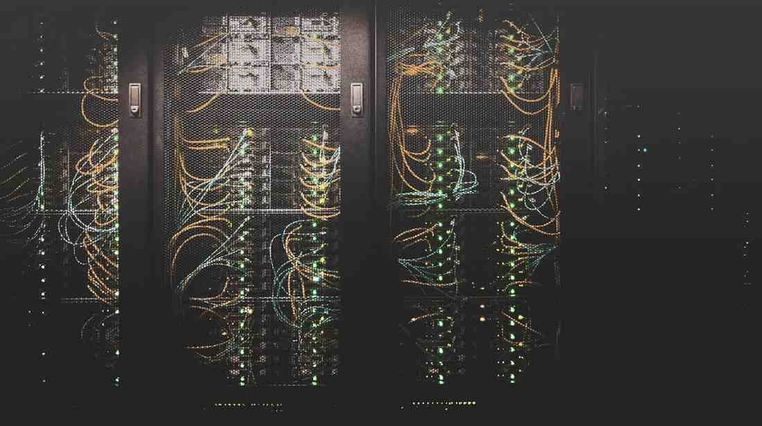 Close-up of a data center's server rack, featuring illuminated network cables in various colors against a dark background.